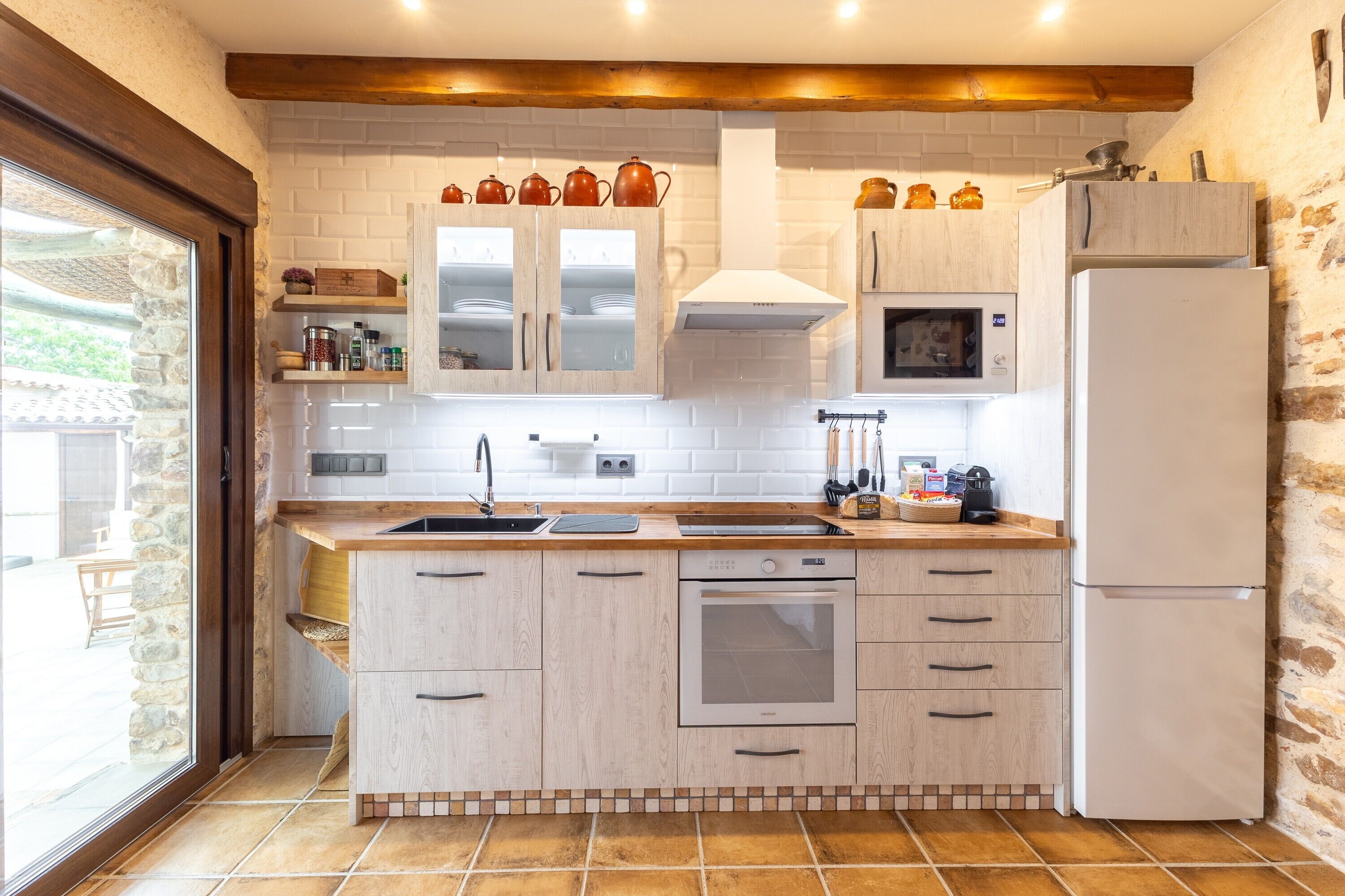 A kitchen with a stone wall, wooden cabinets, a built-in oven, and a refrigerator.