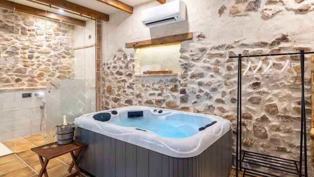 Une salle de bain aux murs de pierre, dotée d’un jacuzzi, de poutres en bois et d’un porte-serviettes.