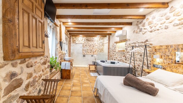 Un baño rústico con pared de piedra, vigas de madera, una bañera y una zona de ducha.