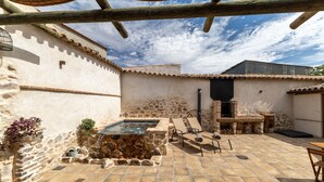 Un patio con paredes de piedra, una piscina de piedra, sillas de descanso, zona de barbacoa y chimenea.