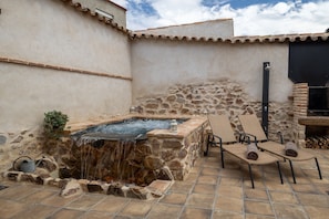 A stone hot tub with a waterfall feature, surrounded by lounge chairs and a stone wall.