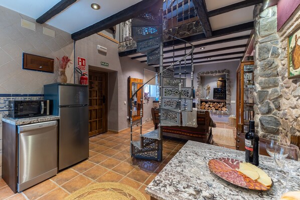 A kitchen with a stainless steel refrigerator, a microwave, and a dishwasher. There is a stone wall with a fireplace and a spiral staircase.