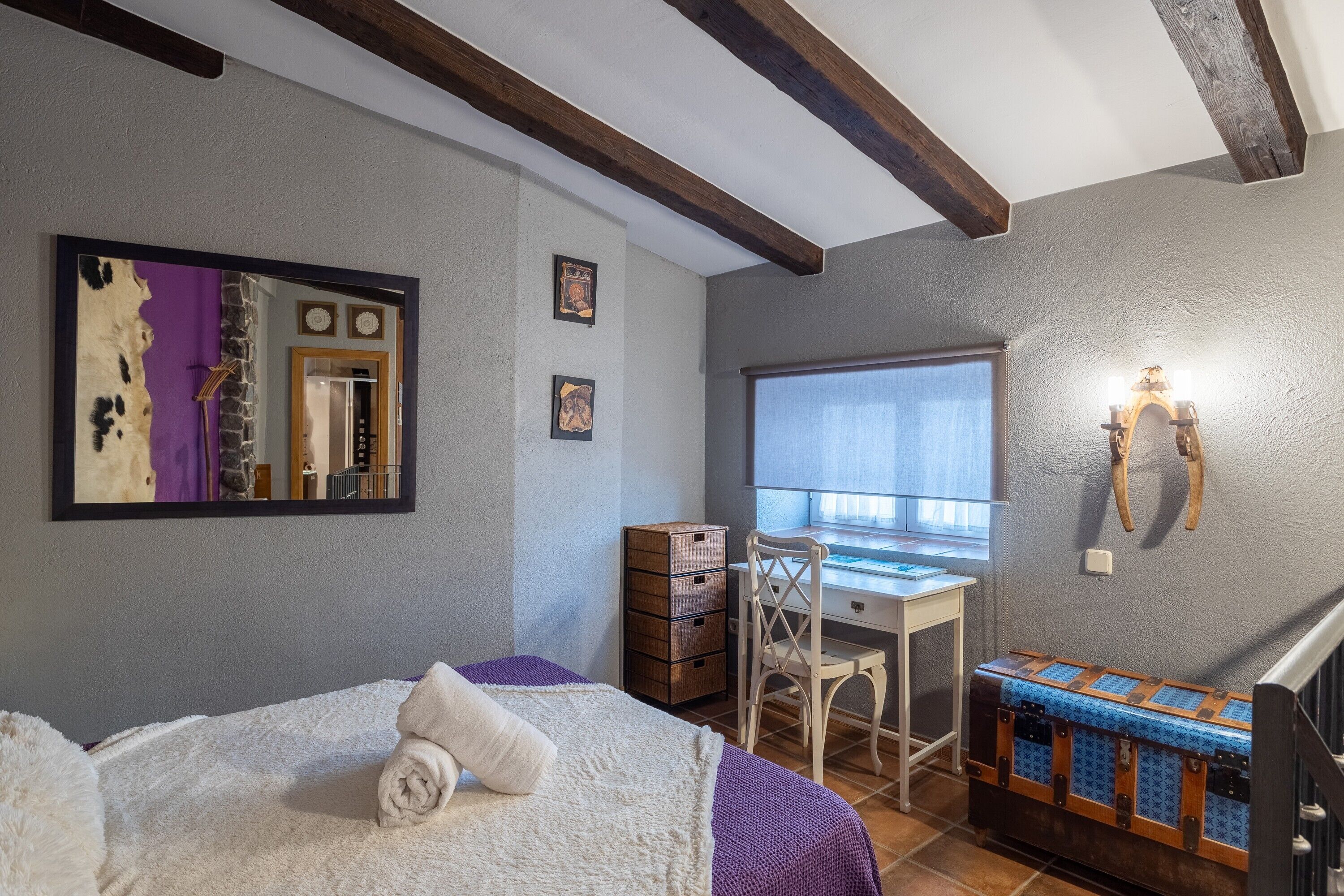 A bedroom with a bed, a desk, a chair, a dresser, and a window.