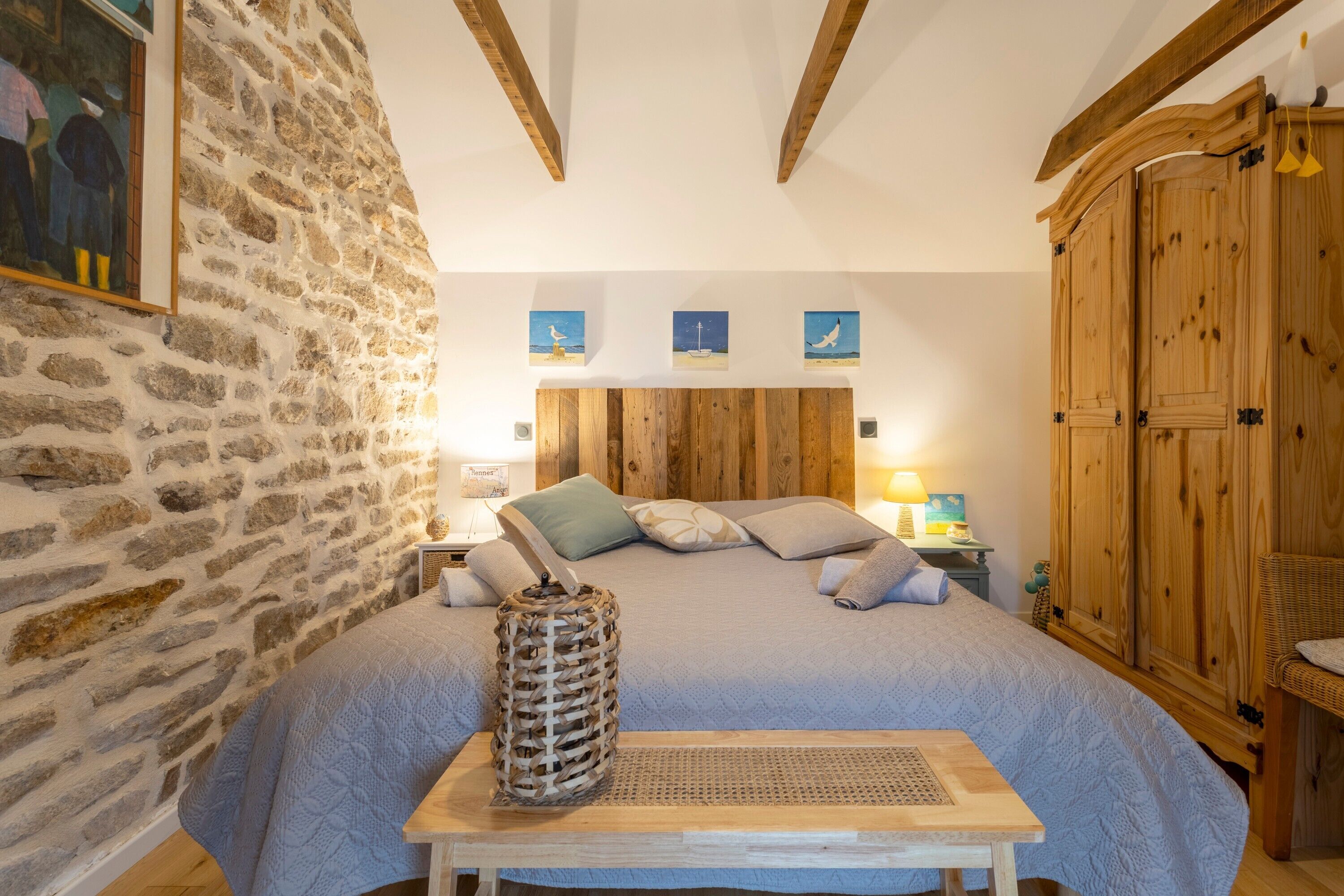 A bedroom with a stone wall, wooden ceiling beams, a bed with a blue quilt, and wooden furniture.