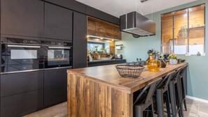 Une cuisine moderne avec des meubles de couleur sombre, un îlot central en bois et des tabourets de bar.