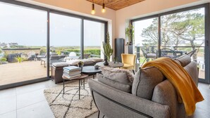 Un salon moderne avec un canapé, une table basse et des fauteuils, de grandes fenêtres et un plafond en bois.