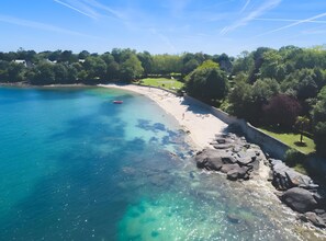 A coastal beach with clear water, a sandy shore, and a rocky outcrop.