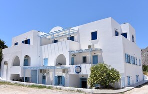Ein weißes Gebäude mit blauen Akzenten, zahlreichen Fenstern und einem kleinen Baum davor.