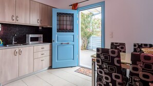 Een keuken met lichte houten kastjes, een blauwe deur en een eethoek met gestreepte stoelen.