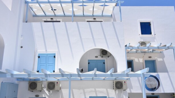 Een wit gebouw met blauwe deuren en ramen, voorzien van airconditioning en een bord met de naam 'Adelphi'.