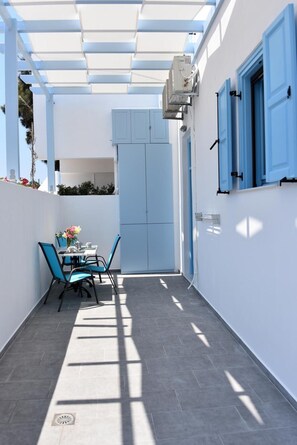 Uma área externa coberta com uma mesa, cadeiras, uma porta e um aparelho de ar condicionado.