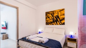 Une chambre à coucher avec un lit, deux tables de chevet avec des lampes, un tableau au mur et un téléviseur posé sur un meuble.
