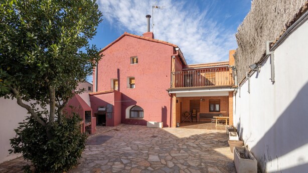 Un patio con suelo de piedra, un edificio rojo con balcón y un árbol.