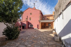 Une cour dallée de pierres, un bâtiment rouge doté d’un balcon et un arbre.
