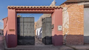 Una entrada con portón metálico, un letrero con un logotipo y un edificio de ladrillo con una puerta de metal corrugado.