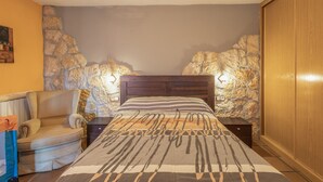 Un dormitorio con una cama, una silla, una mesita de noche, un armario de madera y una pared de piedra.