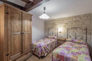 A bedroom with two beds, wooden wardrobe, stone wall, and a hanging light fixture.