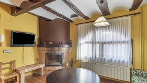 Una sala de estar con chimenea de ladrillo, un televisor montado en la pared, una mesa redonda y un sofá.