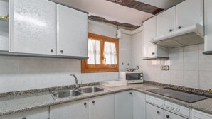Una cocina con armarios blancos, encimera de granito, pileta de acero inoxidable, microondas y estufa.