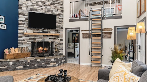 Una sala de estar con chimenea de piedra, televisor de pantalla plana, mesa de centro de madera y sofá gris con almohadones decorativos.
