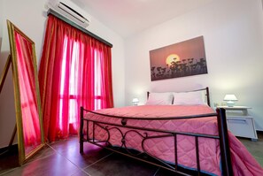 Een slaapkamer met een bed, gordijnen, een schilderij, een nachtkastje en een airconditioner.