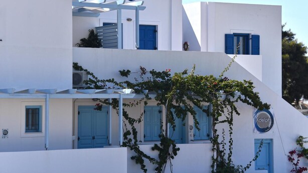 A white building with blue shutters and a circular logo. - Apartment '3  44' with Mountain View, Wi-Fi and Air Conditioning (Santorini)