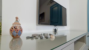 A modern room with a glass-top table, a decorative ceramic vase, a flat-screen TV, and a cabinet. - Apartment '3  44' with Mountain View, Wi-Fi and Air Conditioning (Santorini)