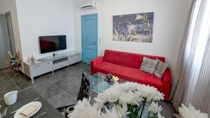A modern living room with a red sofa, a glass coffee table, a flat-screen TV, and a painting on the wall. - Apartment '3  44' with Mountain View, Wi-Fi and Air Conditioning (Santorini)