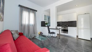 A modern living room with a red sofa, a glass coffee table, and a kitchen area with white cabinets and a refrigerator. - Apartment '3  44' with Mountain View, Wi-Fi and Air Conditioning (Santorini)