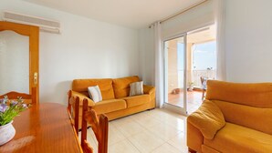Een woonkamer met een bank, een eettafel met stoelen en een schuifpui die uitkomt op een balkon.