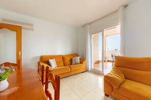Una sala de estar con un sofá, una mesa de comedor con sillas y un ventanal corredero que da a un balcón.