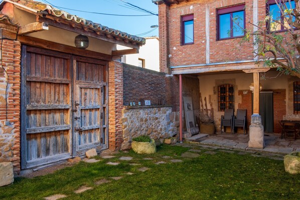 A rustic building with a stone wall, wooden doors, and a small garden area with a stone bench.