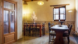 A dining area with a wooden table and chairs, a vase with flowers, a stone wall, and a window with shutters.