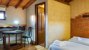 A room with a wooden ceiling, a bed with white linens, a small table with a lamp, and a chair.