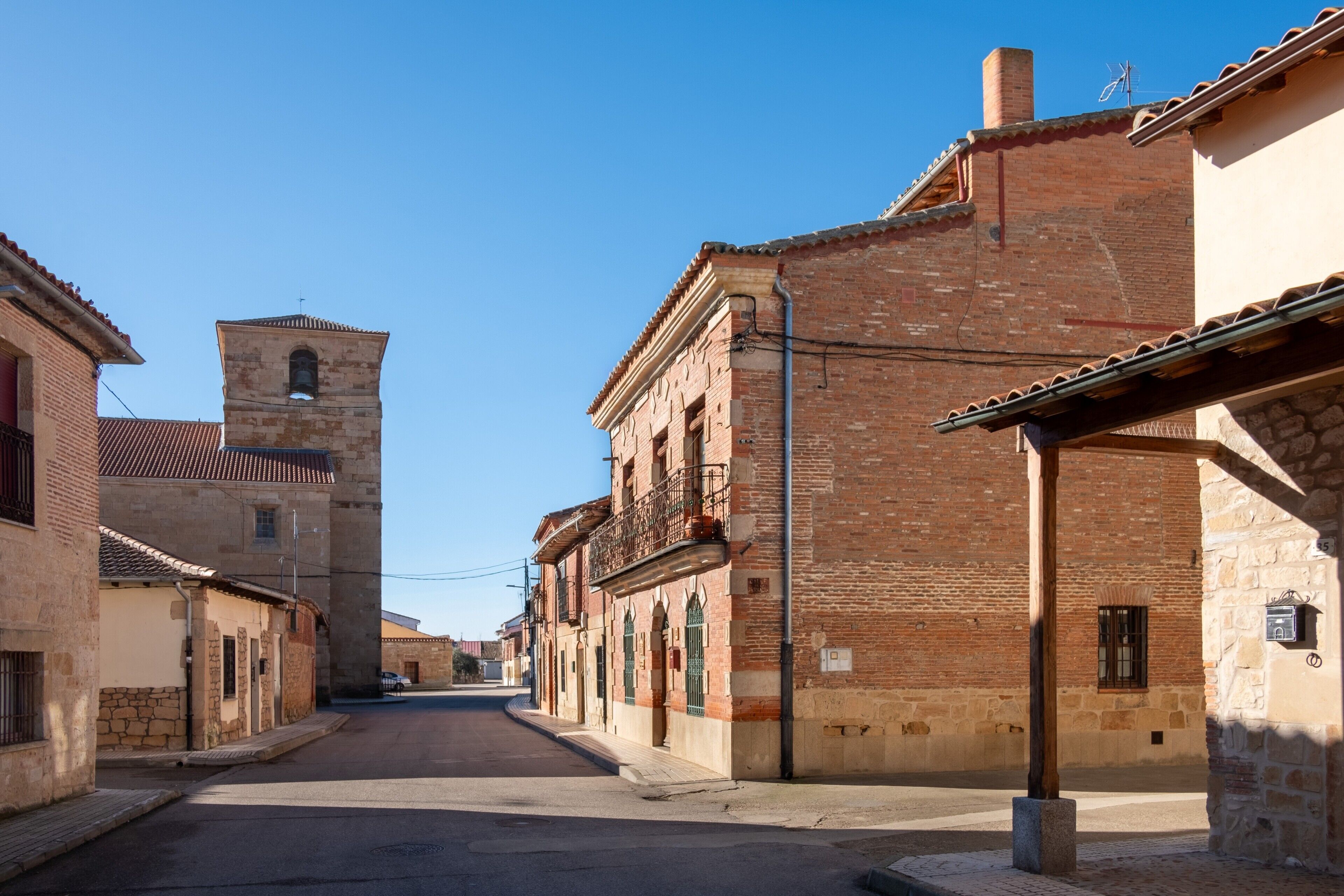 Une rue étroite bordée de bâtiments historiques, une tour imposante et un ciel d’un bleu éclatant.