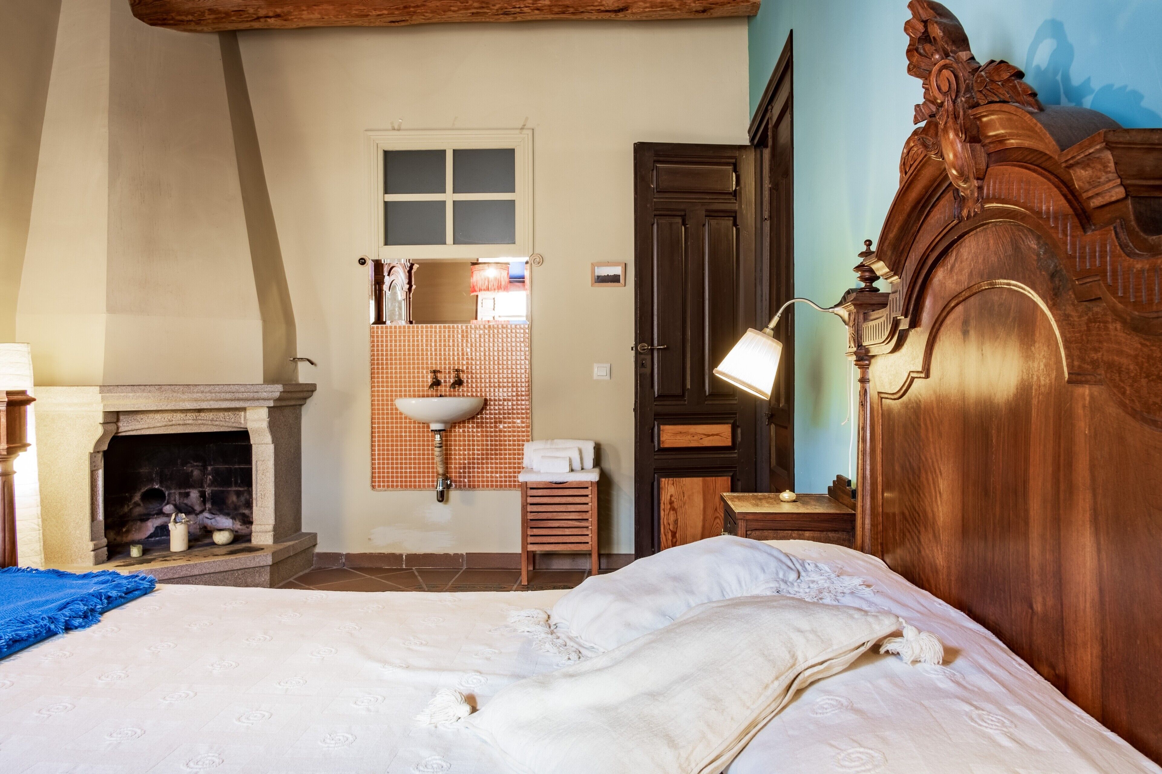 A bedroom with a bed, a fireplace, a wooden wardrobe, a mirror, and a sink.