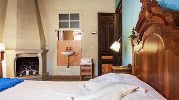 A bedroom with a bed, a fireplace, a wooden wardrobe, a mirror, and a sink.