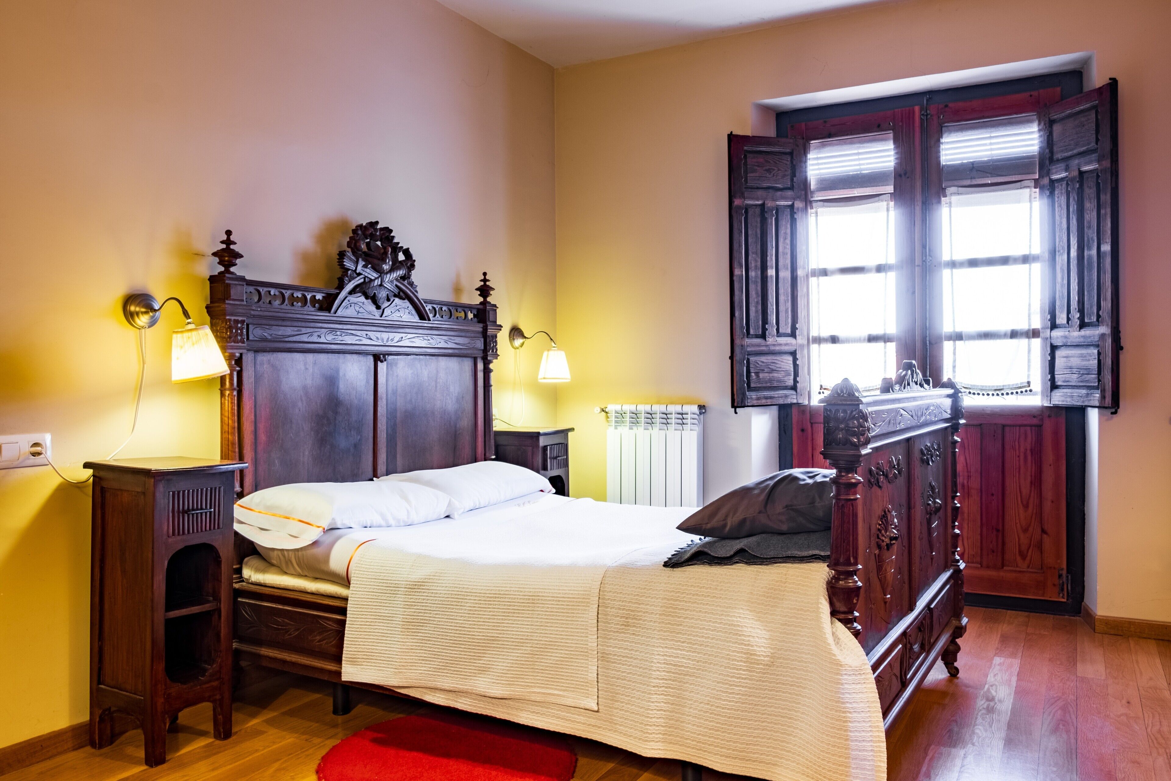 Une chambre à coucher avec un lit en bois, des lampes de chevet, un radiateur et une fenêtre avec des volets.