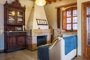 A room with a fireplace, a cabinet, a sofa, and a window with wooden shutters.
