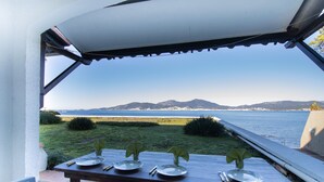 Mesa de comedor dispuesta con platos y cubiertos, con vistas a un paisaje costero con montañas y el mar.