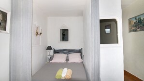 Un dormitorio con cama, mesita de noche, lámpara, ventana y un cuadro en la pared.