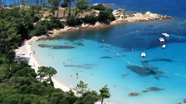 Una playa costera con aguas turquesas cristalinas, afloramientos rocosos y una orilla arenosa.