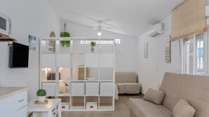 A modern living room with a white sofa, a white cabinet with shelves, a ceiling fan, and a window with blinds.