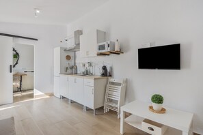 Una cocina moderna con armarios blancos, microondas y televisor montado en la pared.