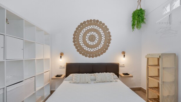 A bedroom with a bed, bedside tables, a wall-mounted decorative piece, and built-in shelving.