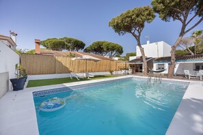 Una piscina con un flotador, rodeada de sillones de descanso y un pequeño jardín.