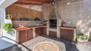An outdoor kitchen area with a brick wall, wooden ceiling, and a woven rug.