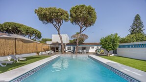 A swimming pool with a tiled border, surrounded by a grassy area and trees.