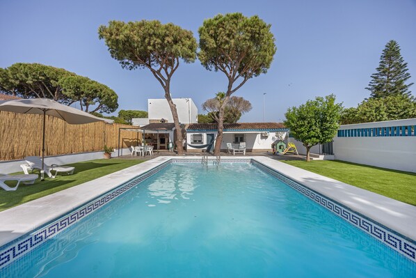 Una piscina con borde de baldosas, rodeada de césped y árboles.