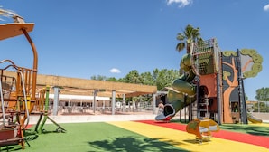 Un parque infantil con tobogán, estructuras para escalar y una zona de estar techada.